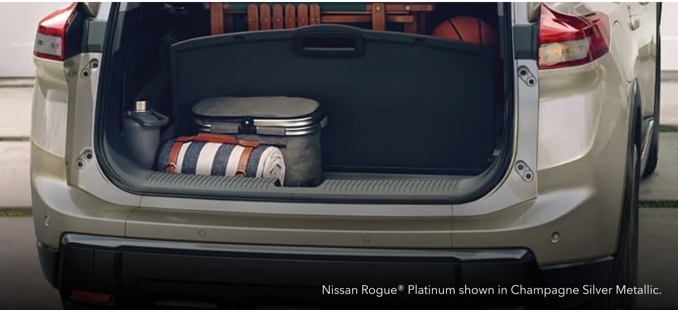 Close-up rear view of an open cargo trunk on a Champagne Silver Nissan Rogue Platinum loaded with outdoor gear in a driveway.