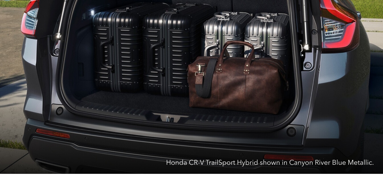 Close-up view of the open cargo area of a Canyon River Blue Honda CR-V TrailSport Hybrid loaded with luggage parked in a sunny driveway.