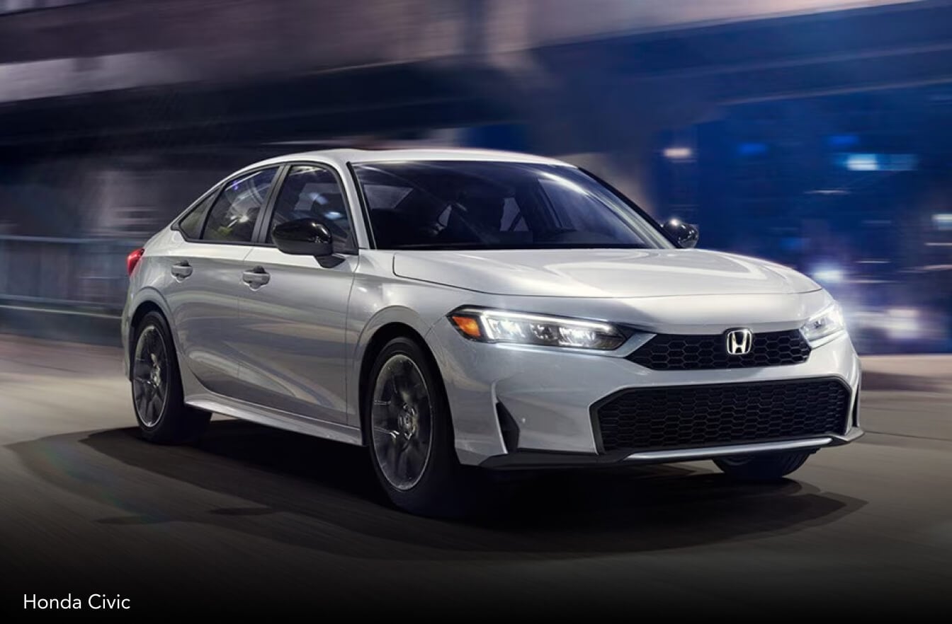 Exterior action shot of a white 2026 Honda Civic driving down an urban street at night.