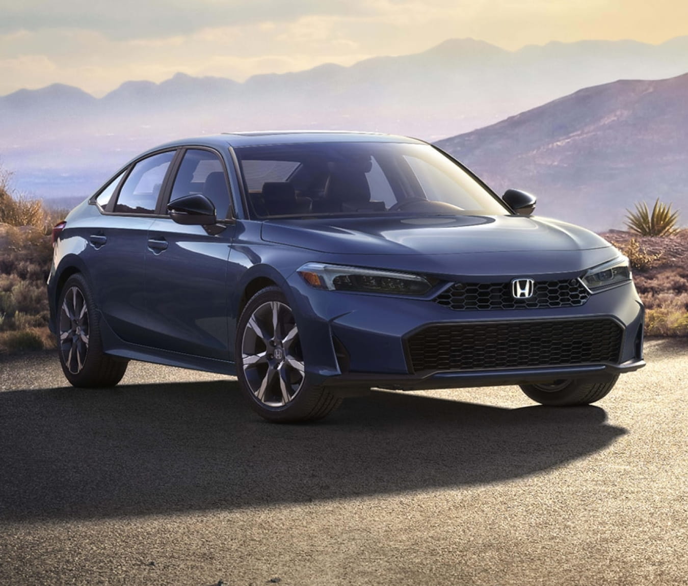 2026 Honda Civic Sedan Hybrid parked on a road with a mountain backdrop at sunset.