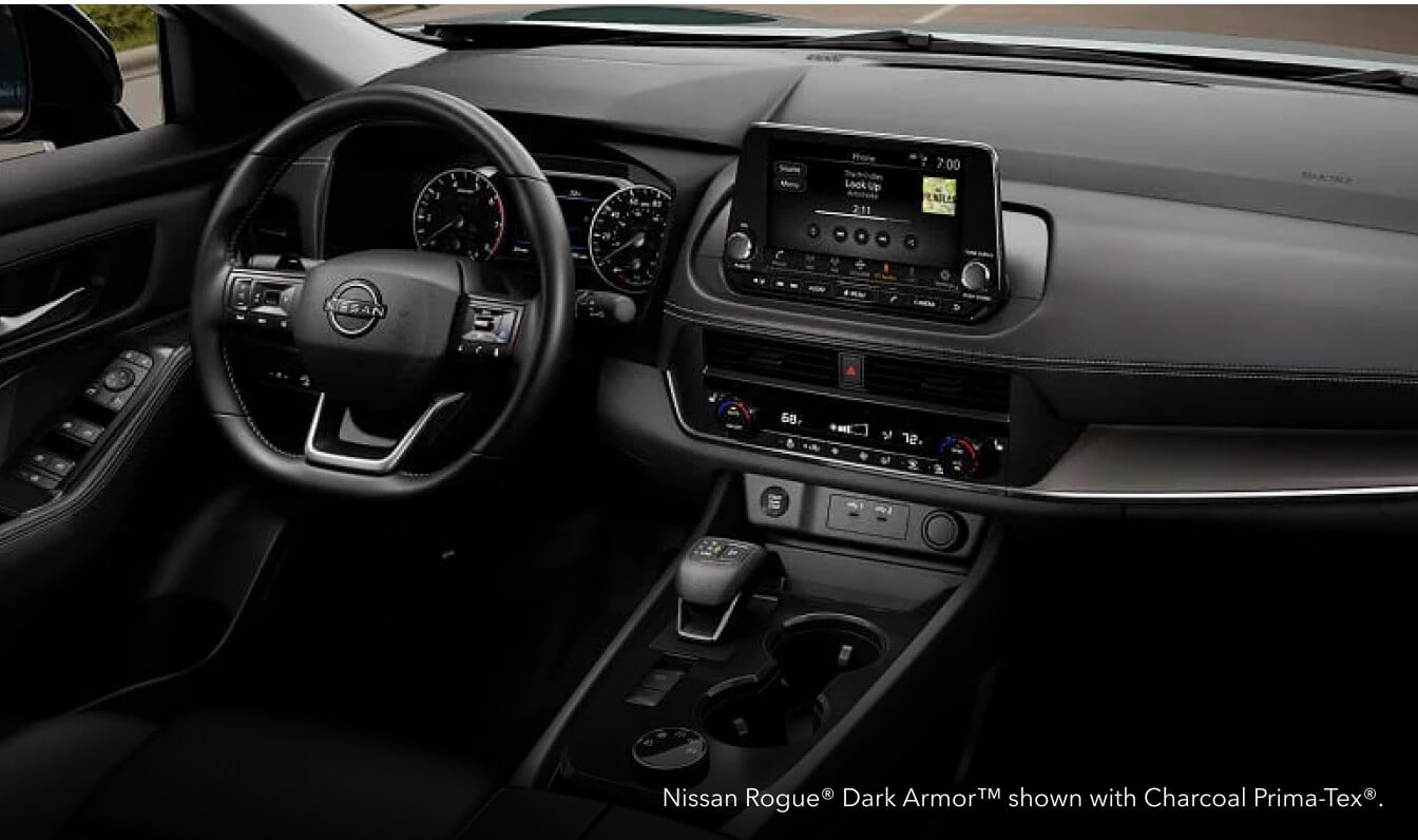 Driver-side cockpit view of a Nissan Rogue Dark Armor dashboard showing the glowing center touchscreen with Charcoal Prima-Tex interior.