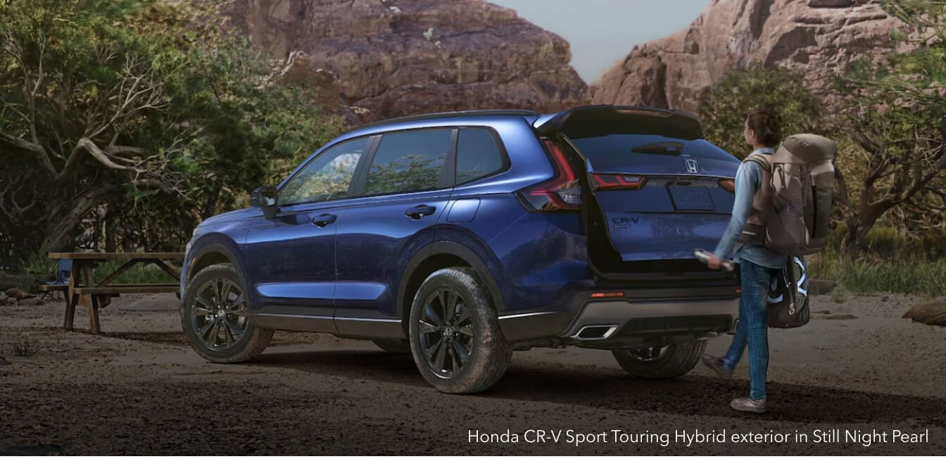 Honda CR-V Sport Touring Hybrid exterior in Still Night Pearl with power tailgate on a wooded campsite.