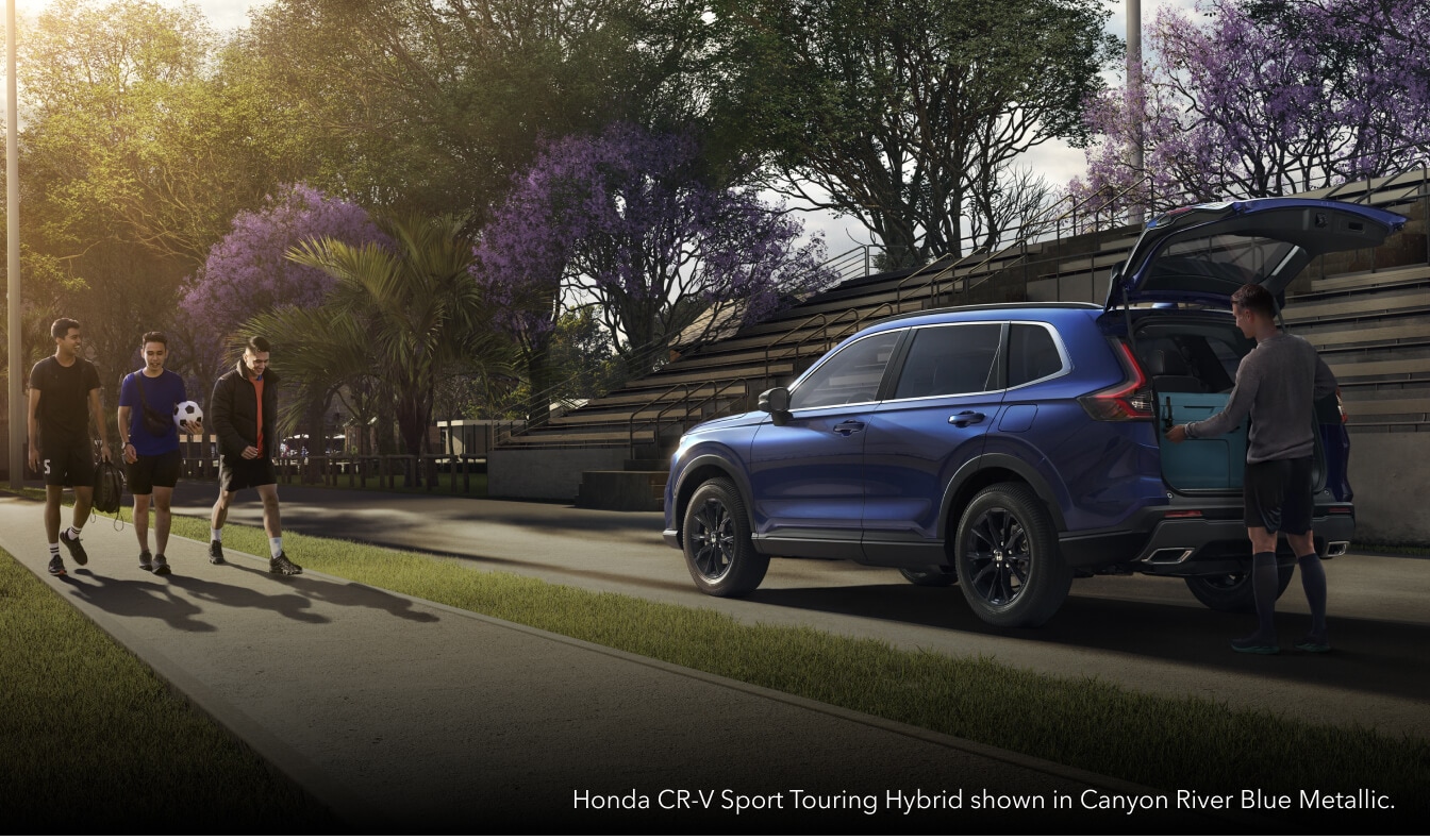 Rear three-quarter view of a Canyon River Blue Honda CR-V Sport Touring Hybrid with an open liftgate next to a sports fi