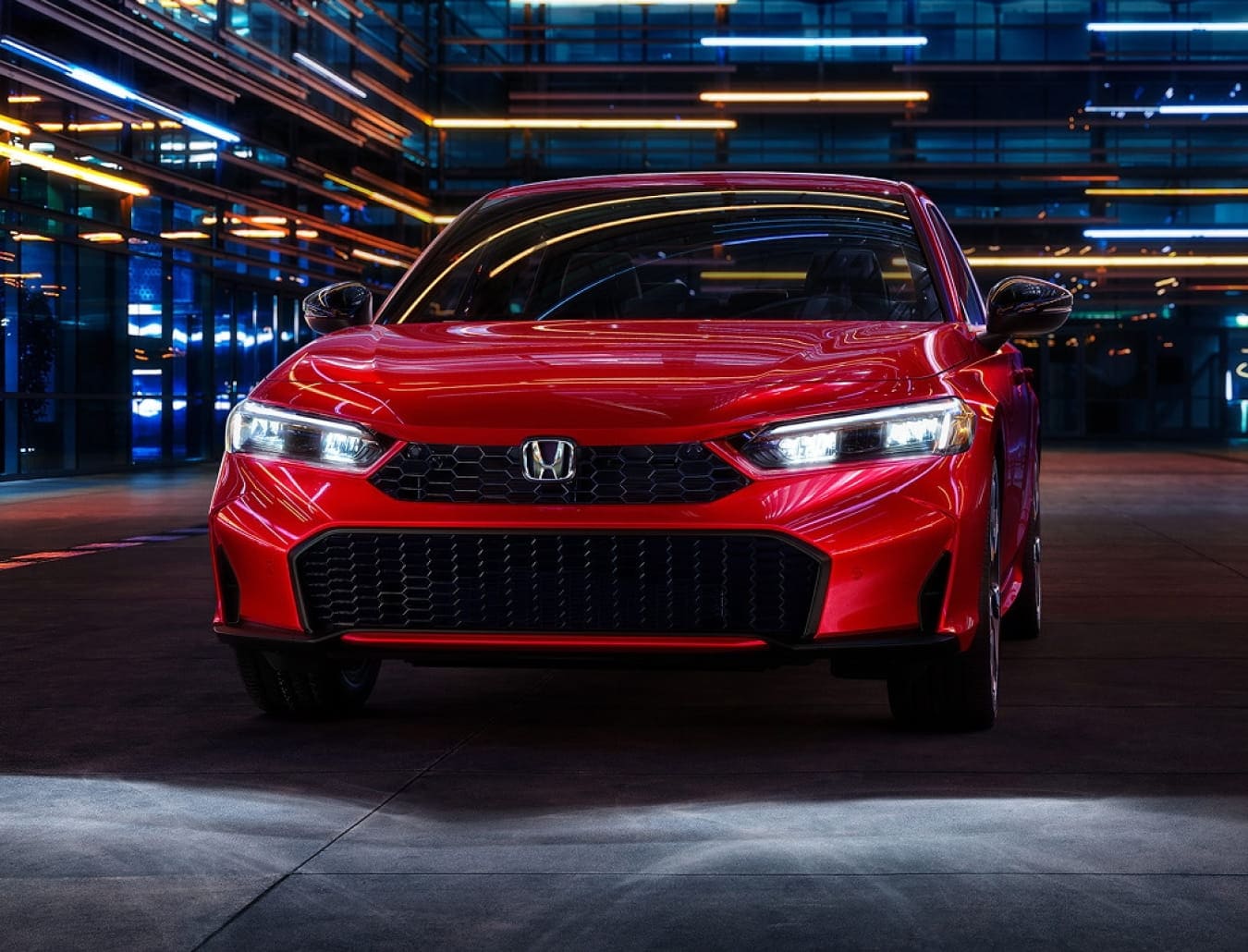 Front view of a 2026 Honda Civic Sedan Hybrid set in an urban area with building lights reflecting on the body.