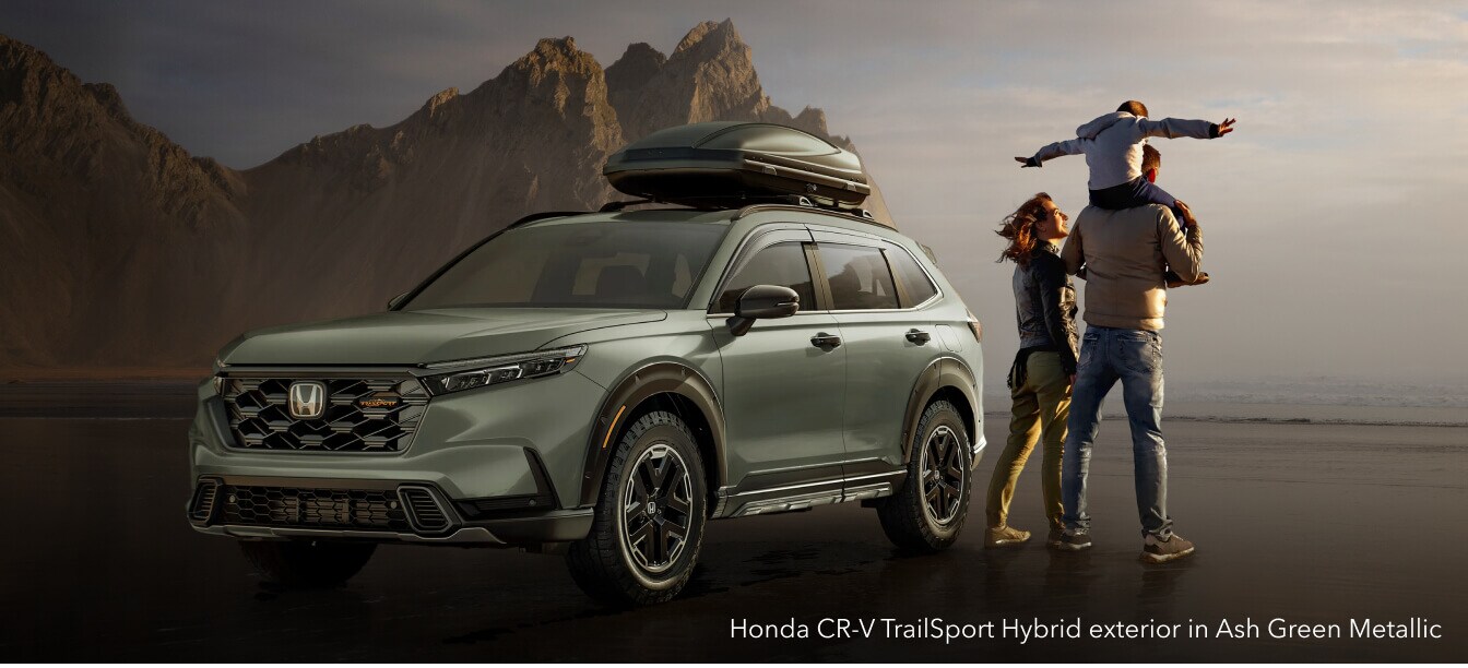 Honda CR-V TrailSport Hybrid exterior in Ash Green Metallic with roof cargo box on a sandy beach.