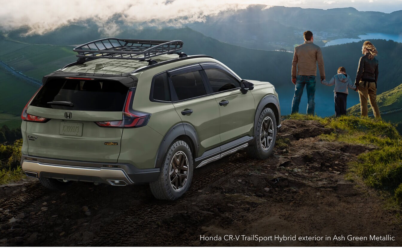 Honda CR-V TrailSport Hybrid exterior in Ash Green Metallic with roof cargo basket on a mountain overlook.