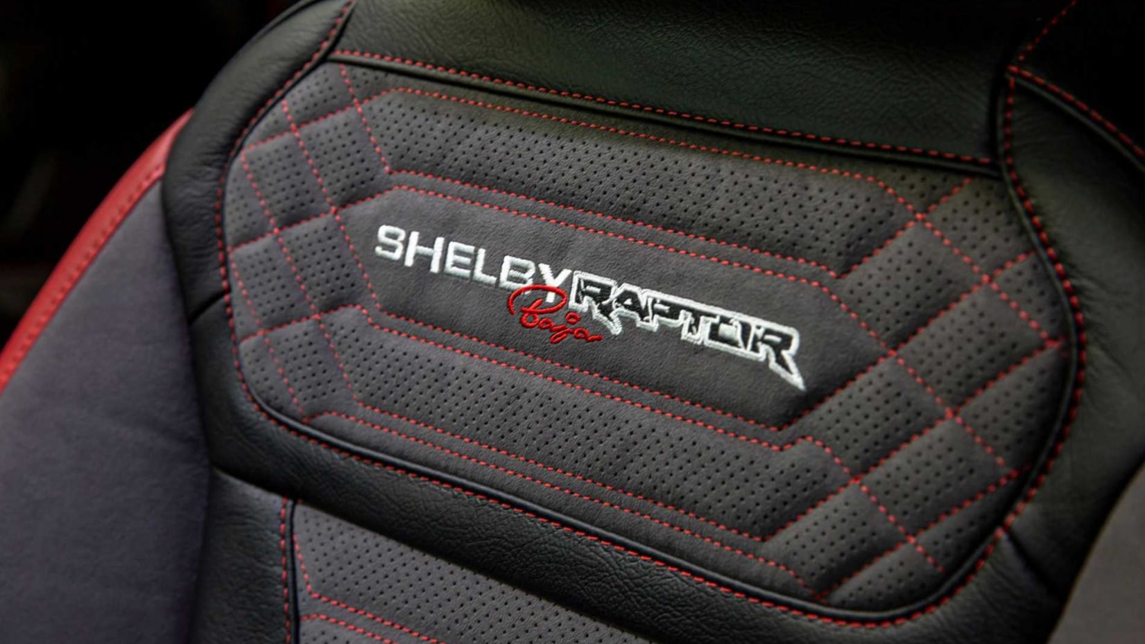 A close up of the quilted gray fabric and leather with red contrast stitching on a seat in the 2022 Ford Shelby Baja Raptor F-150 with Shelby Baja Raptor embroidered near the top