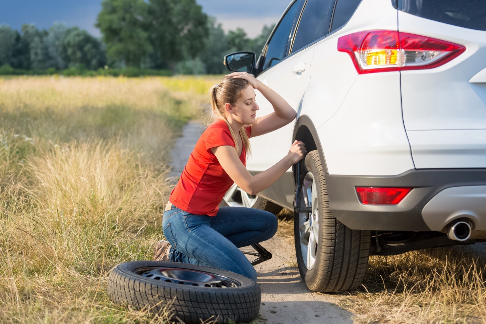 A woman trying to change a tire on a country road