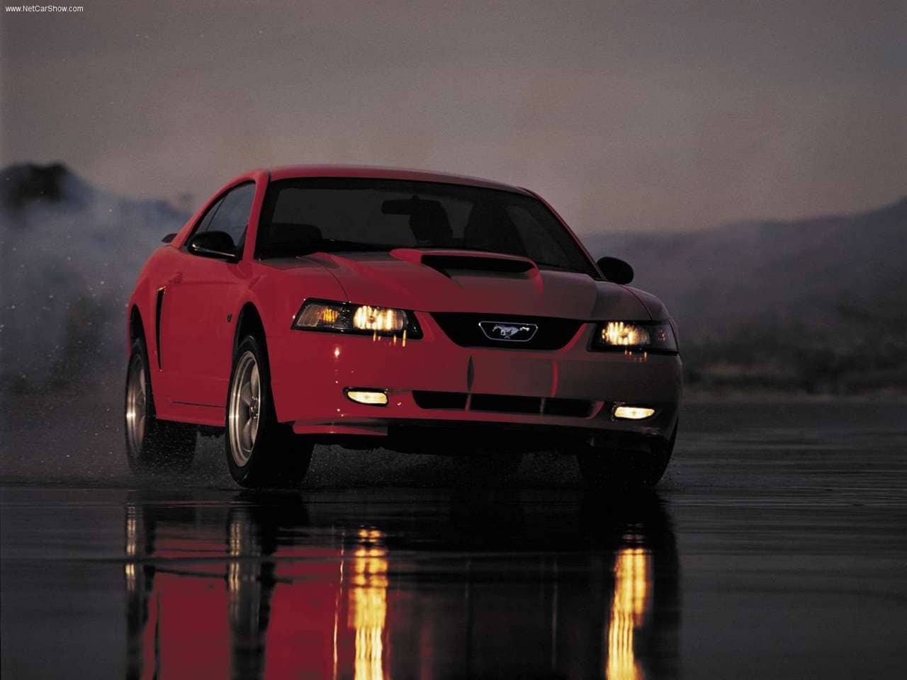 A red 2003 Ford Mustang driving on a track.