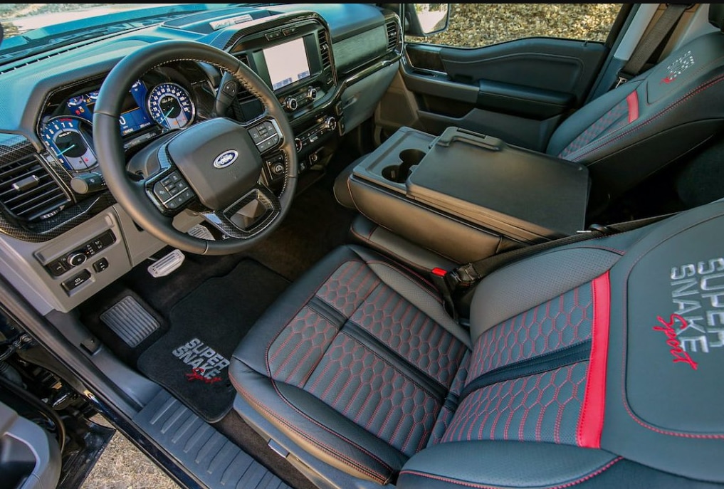 A view of the interior cabin of the 2022 Ford Shelby F-150 Super Snake with monogrammed gray leather seats with red contrast stitching, monogrammed floormats, a large center console, and all digital dash