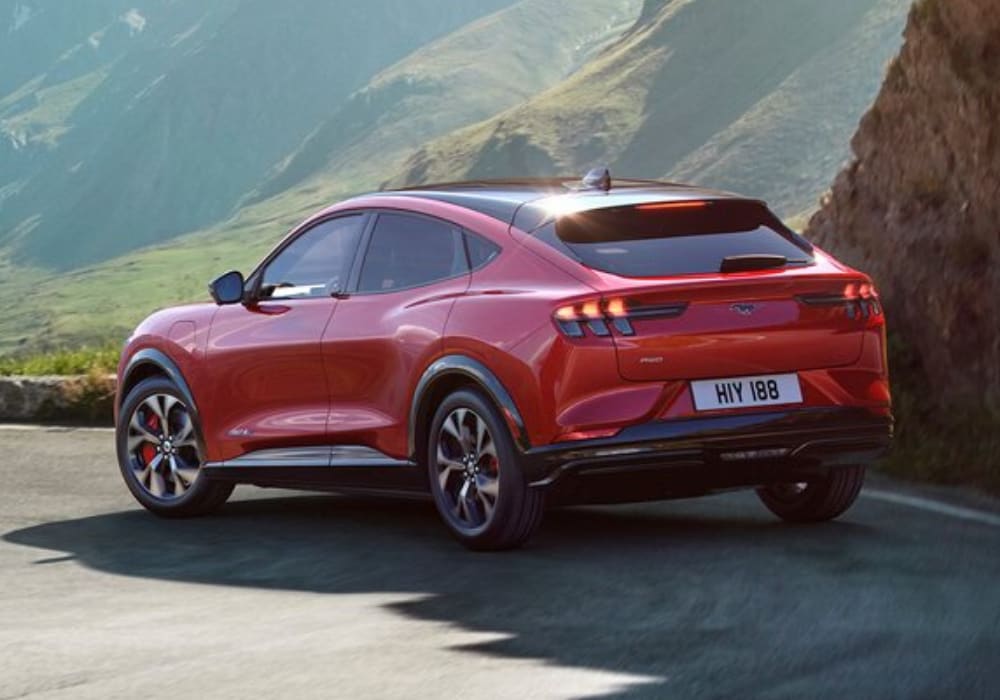 Rear exterior design view of a 2021 Ford Mustang Mach-E in red color going down a curvy mountain-side highway