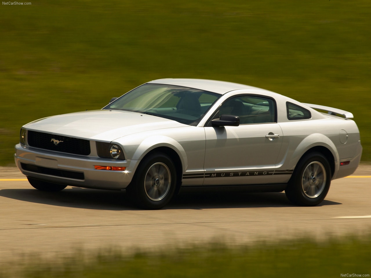 A silver 2005 Ford Mustang driving quickly down a road.