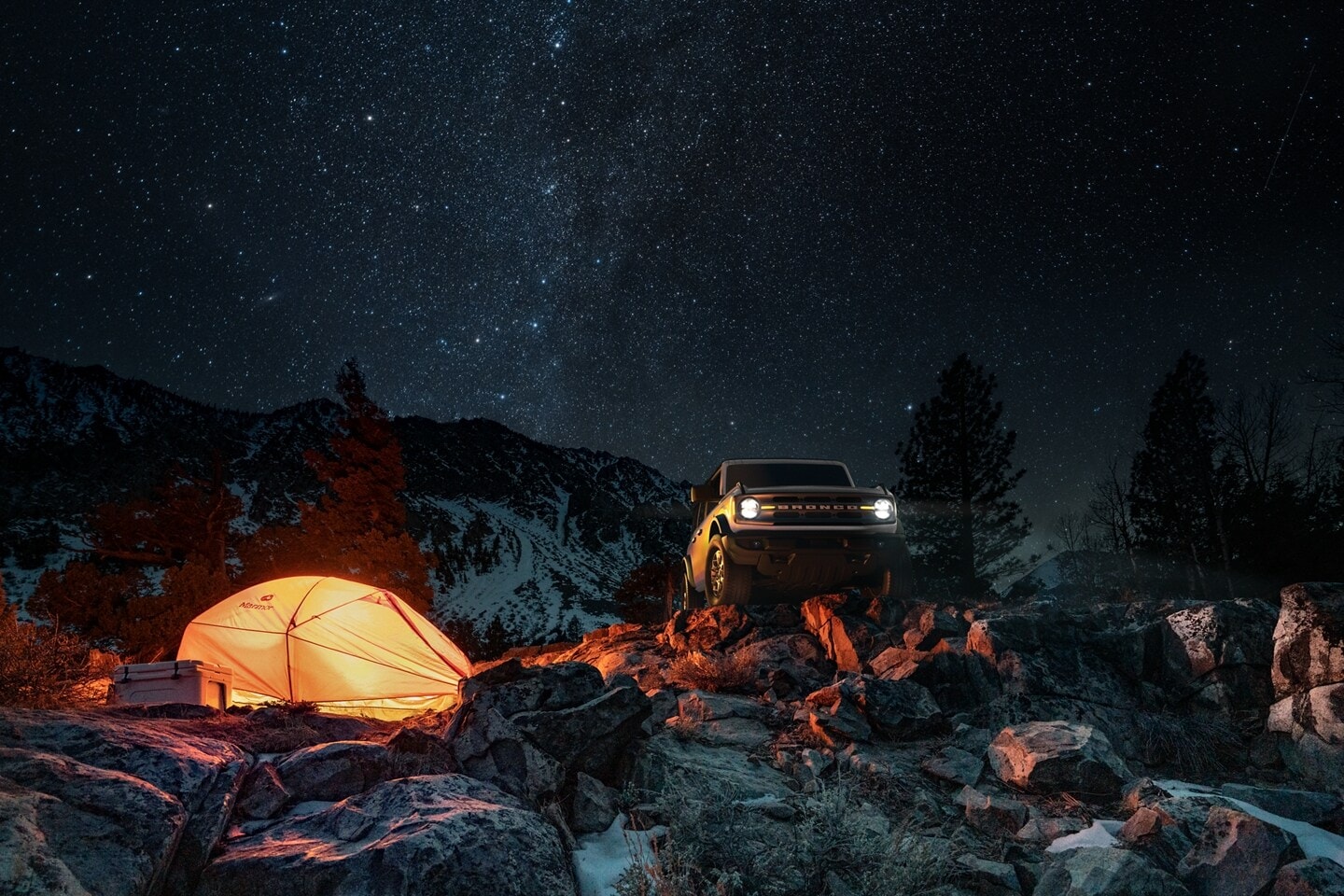 A Ford Bronco parked it the wilderness with a starry sky behind it.