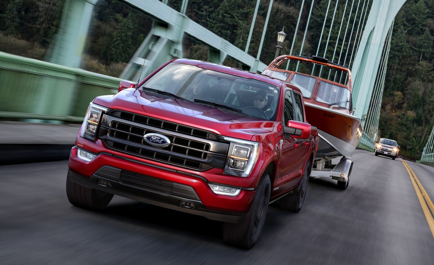 2021 Ford F-150 Truck (2).png New 2021 Ford F-150 3.5L PowerBoost Hybrid in red exterior color pulling a boat over a bridge ahead of the 2020 Ford F-150 in the distance