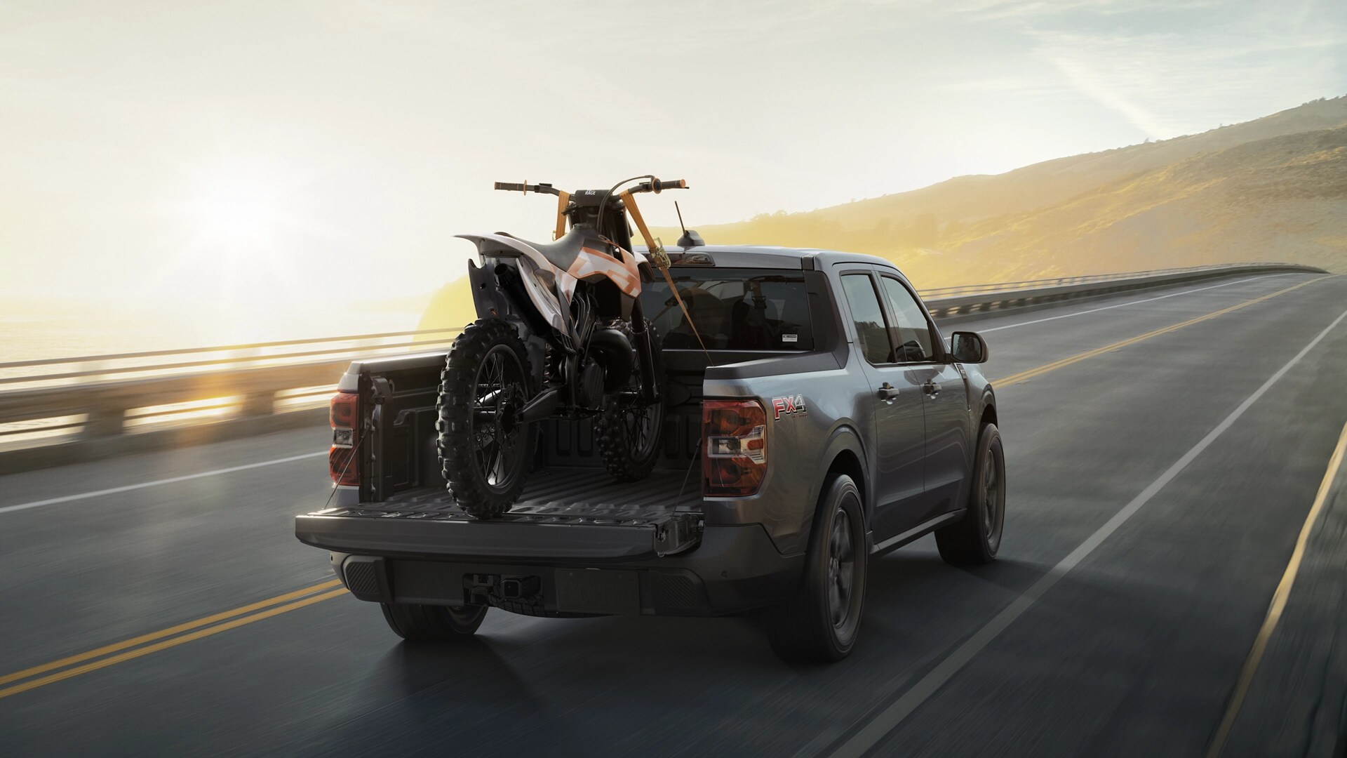 2025 Ford Maverick driving with a dirt bike in the rear bed