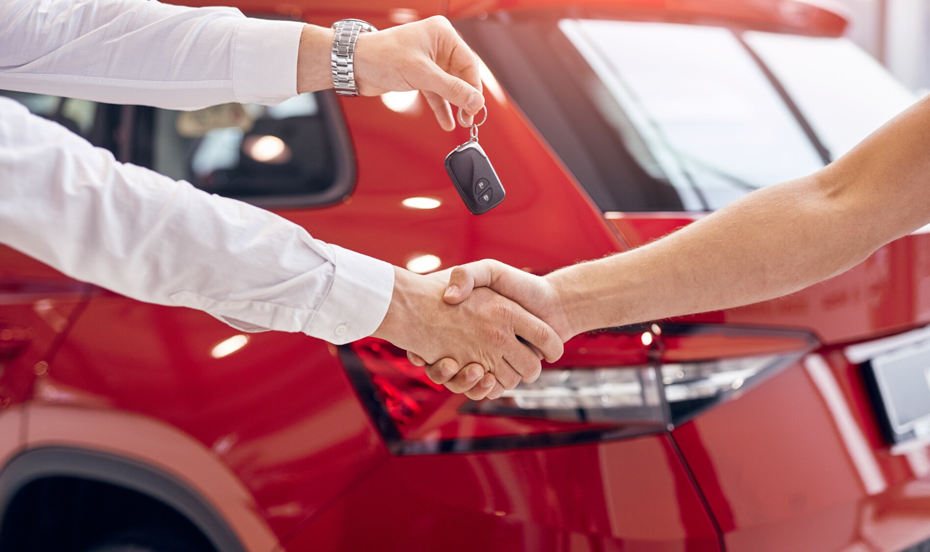 A closeup of a car sales person and a customer as they shake hands and the salesman hands over the keys to a new car