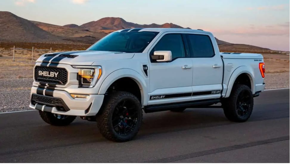 As the sun sets in the desert, a white with black racing stripes 2022 Ford F150 Shelby is parked at an angle showing the side of the truck and the word SHELBY on the grille