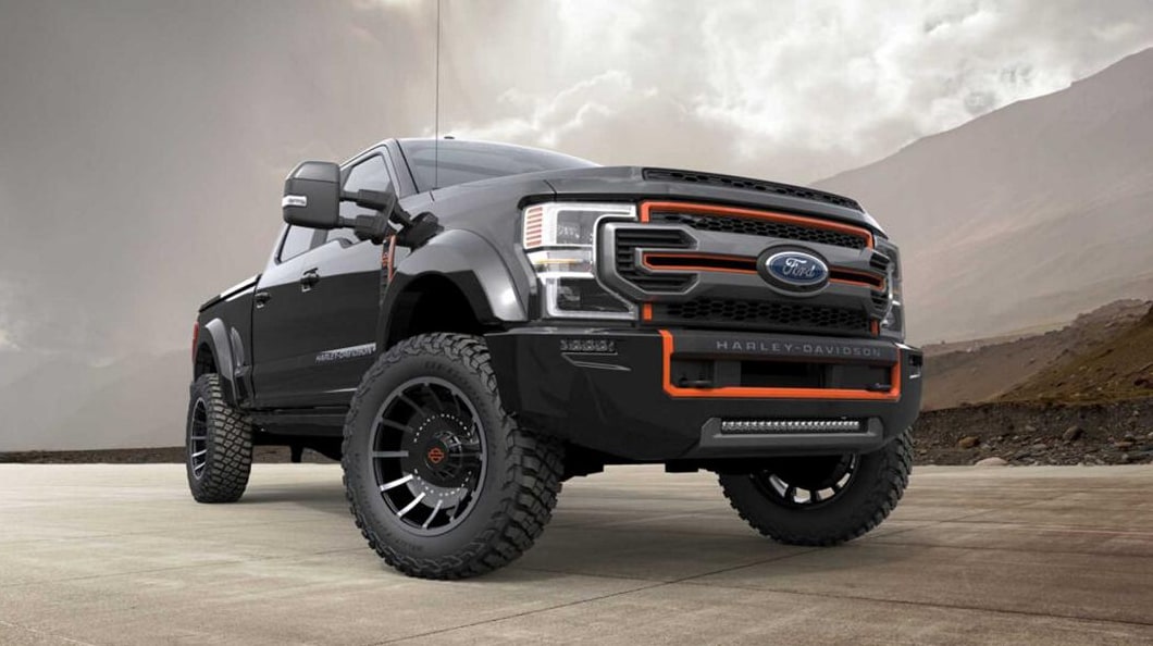 A view of the 2022 Ford F250 Super Duty Harley Davidson as it is parked on an angle on a concrete pad in a barren landscape, with a view of the grille and orange outline detailing on the front
