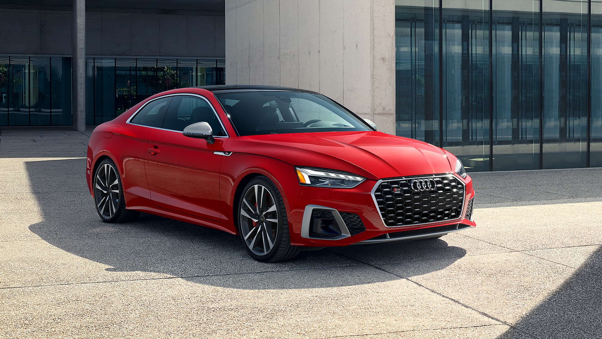 A red Audi A5 parked in front of a modern building.