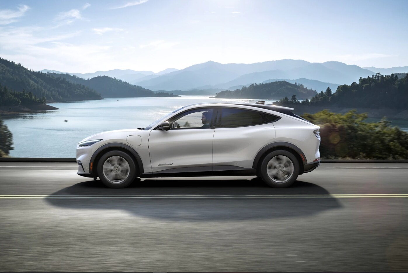 A profile view of a white 2023 Ford Mustang Mach-E driving on a country road