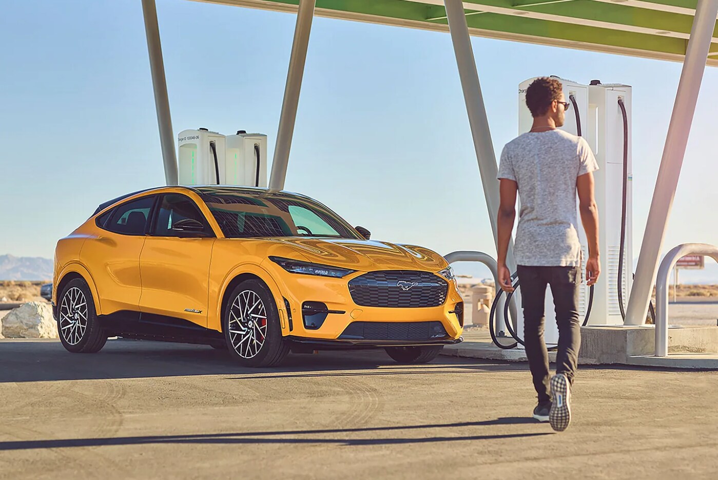 A man walks towards a yellow 2023 Ford Mustang Mach-E parked at a charging station