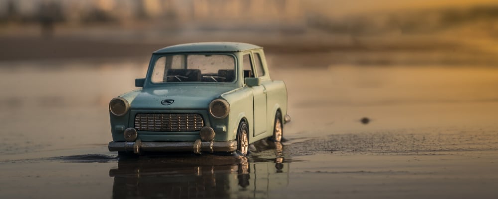 Miniature toy car model stuck in wet sand on the shore of a beach