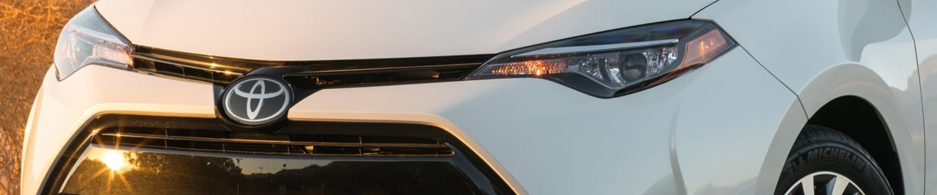 Close up angle of the front grille on a white used Toyota Corolla as the sun glares of the front bumper