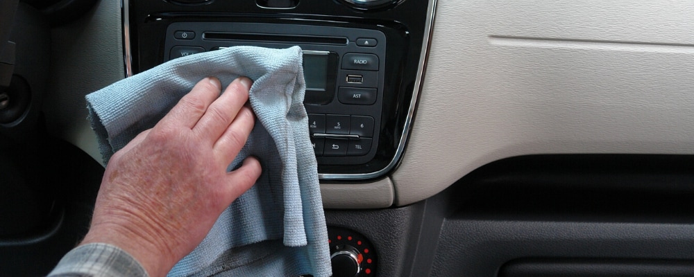 A gentleman cleaning and sanitizing the interior of a car with a microfiber cloth