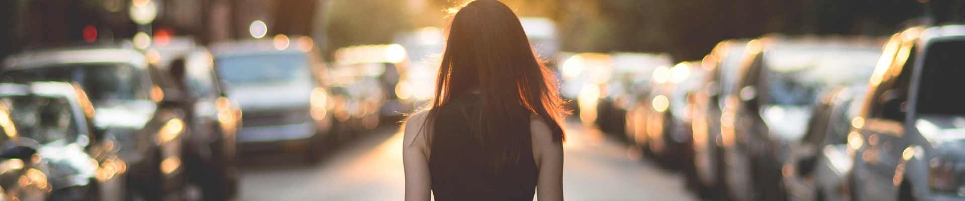 Young woman looking down a row of used cars