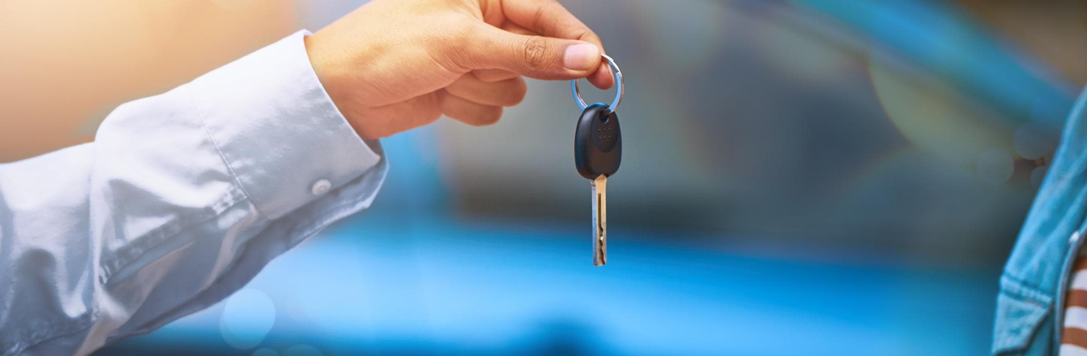 A car salesman handing the keys of a newly purchased car over the the new owner