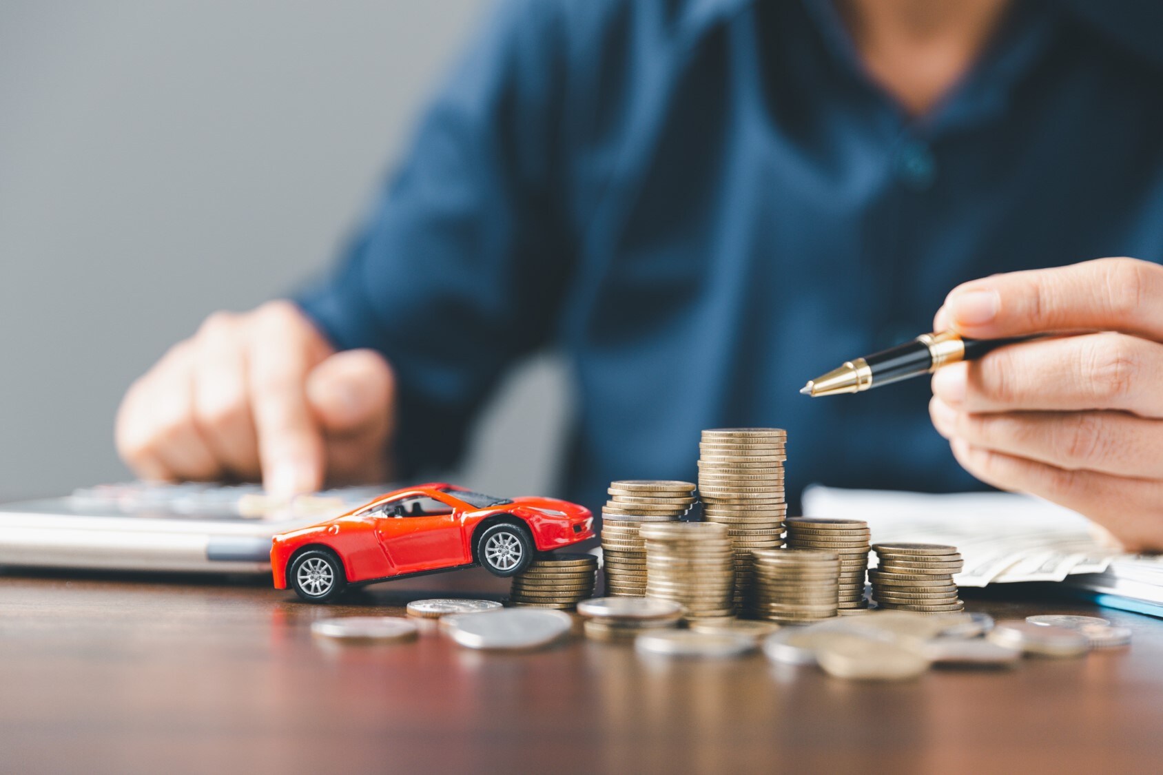 A red toy car on top of a stack of quarters.