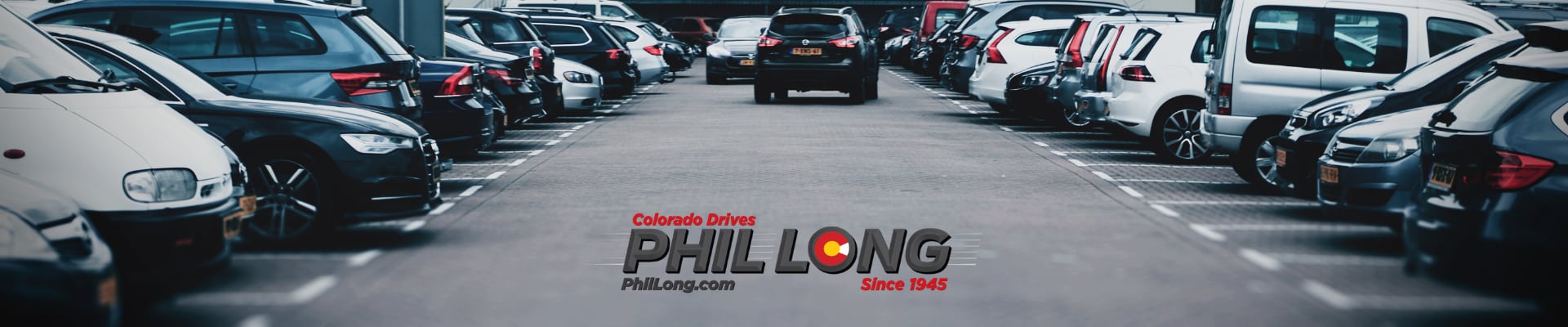 Used car parking lot with many different used cars, used trucks, and used SUVs with Phil Long Dealerships logo front and center