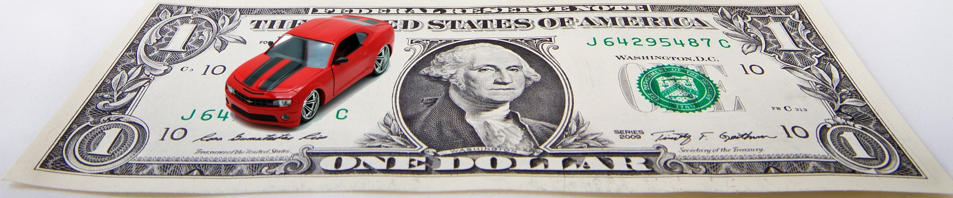 Close up of a dollar bill with a toy Chevy Camaro car sitting atop the dollar
