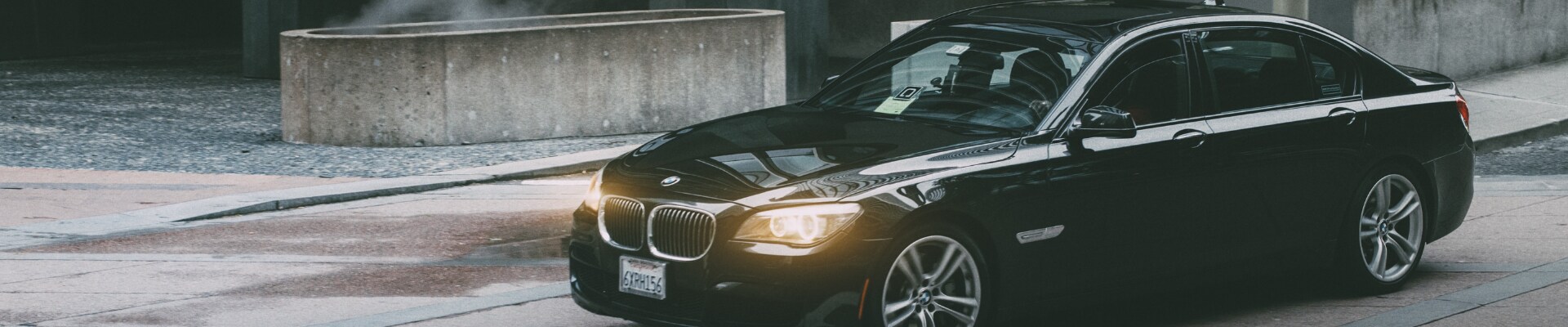 Black used BMW making a right turn on a damp city street on a cold day under a bridge overpass in the evening headlights shining
