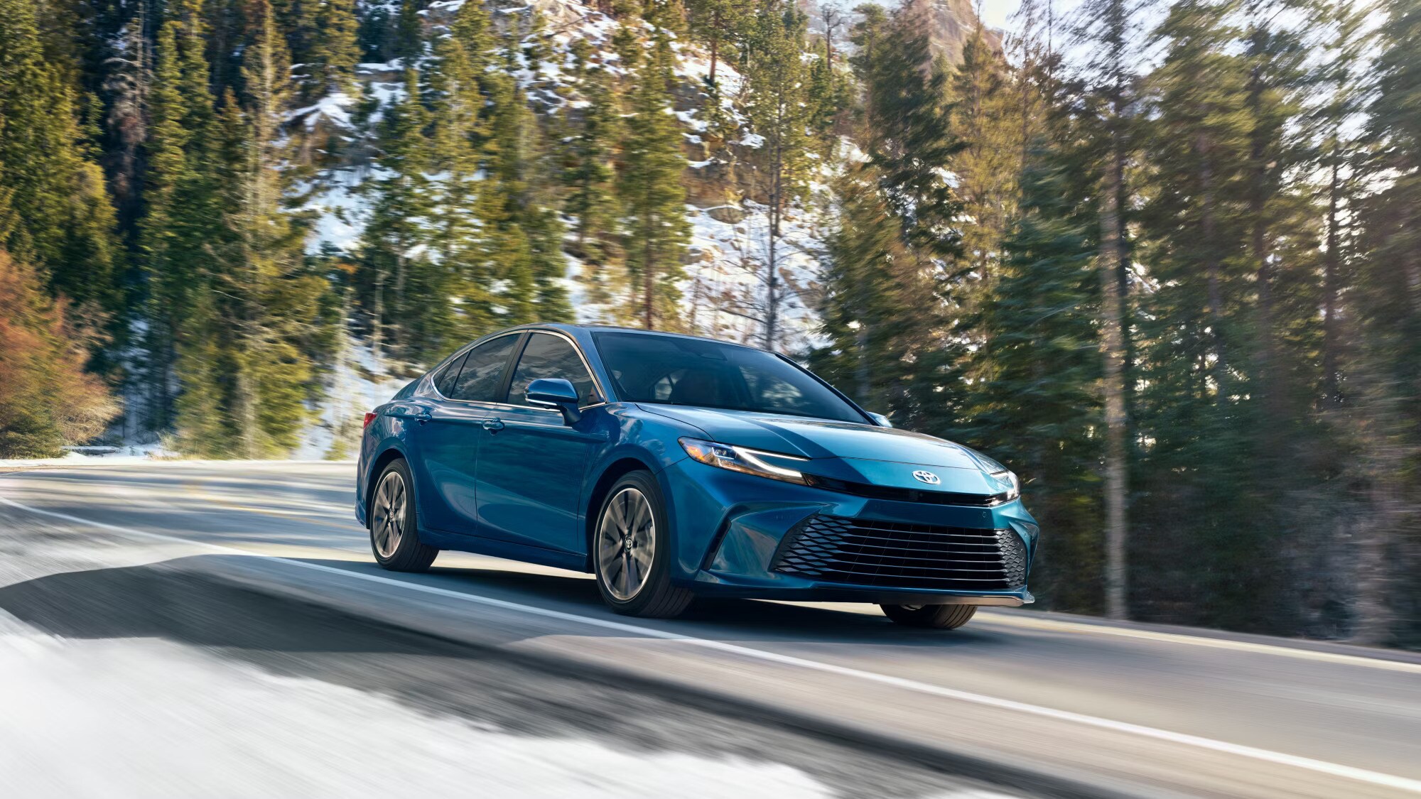A blue 2025 Toyota Camry driving on a mountain highway.