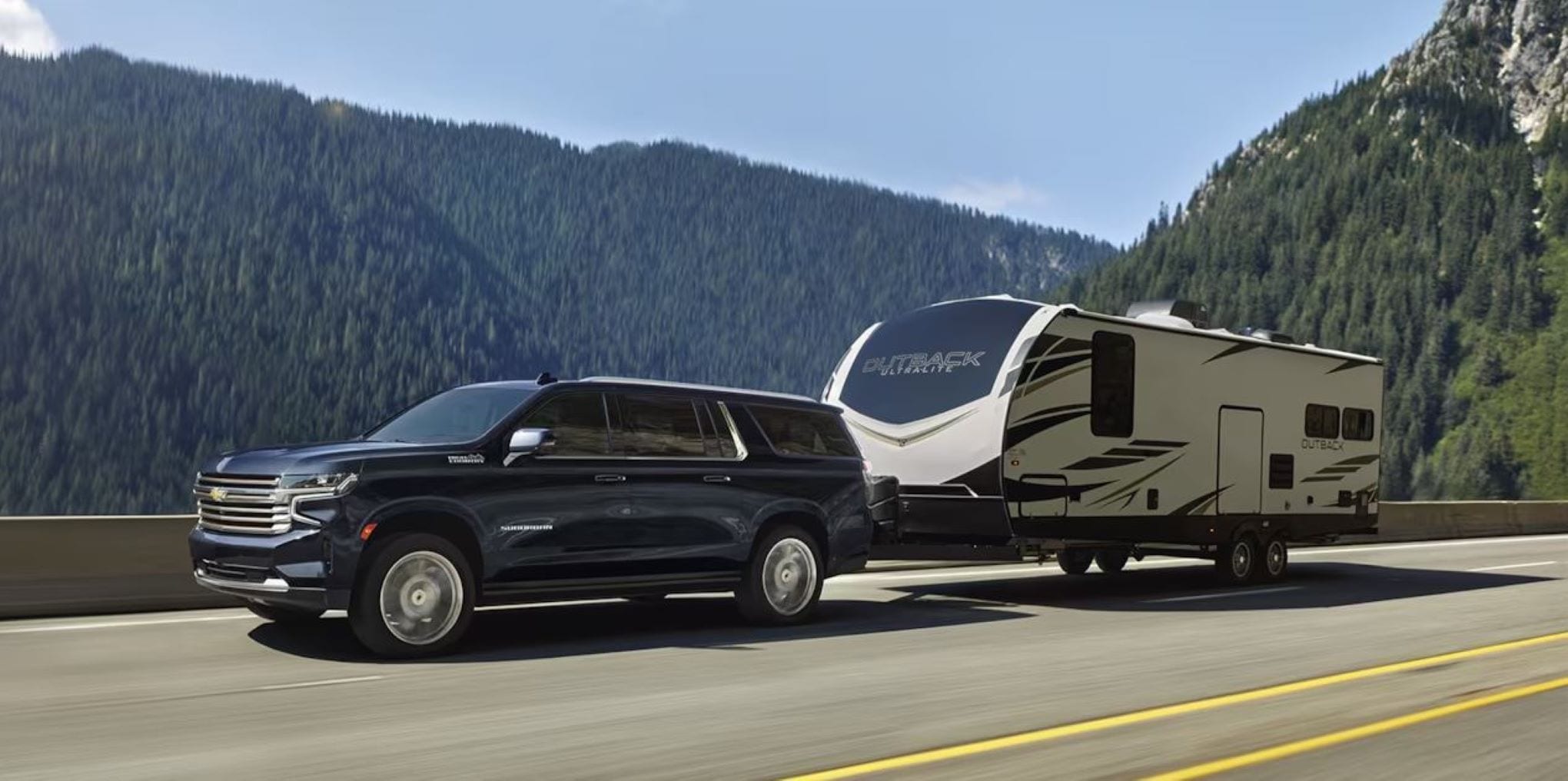 A Chevy Suburban pulling a large camper behind it.' class=