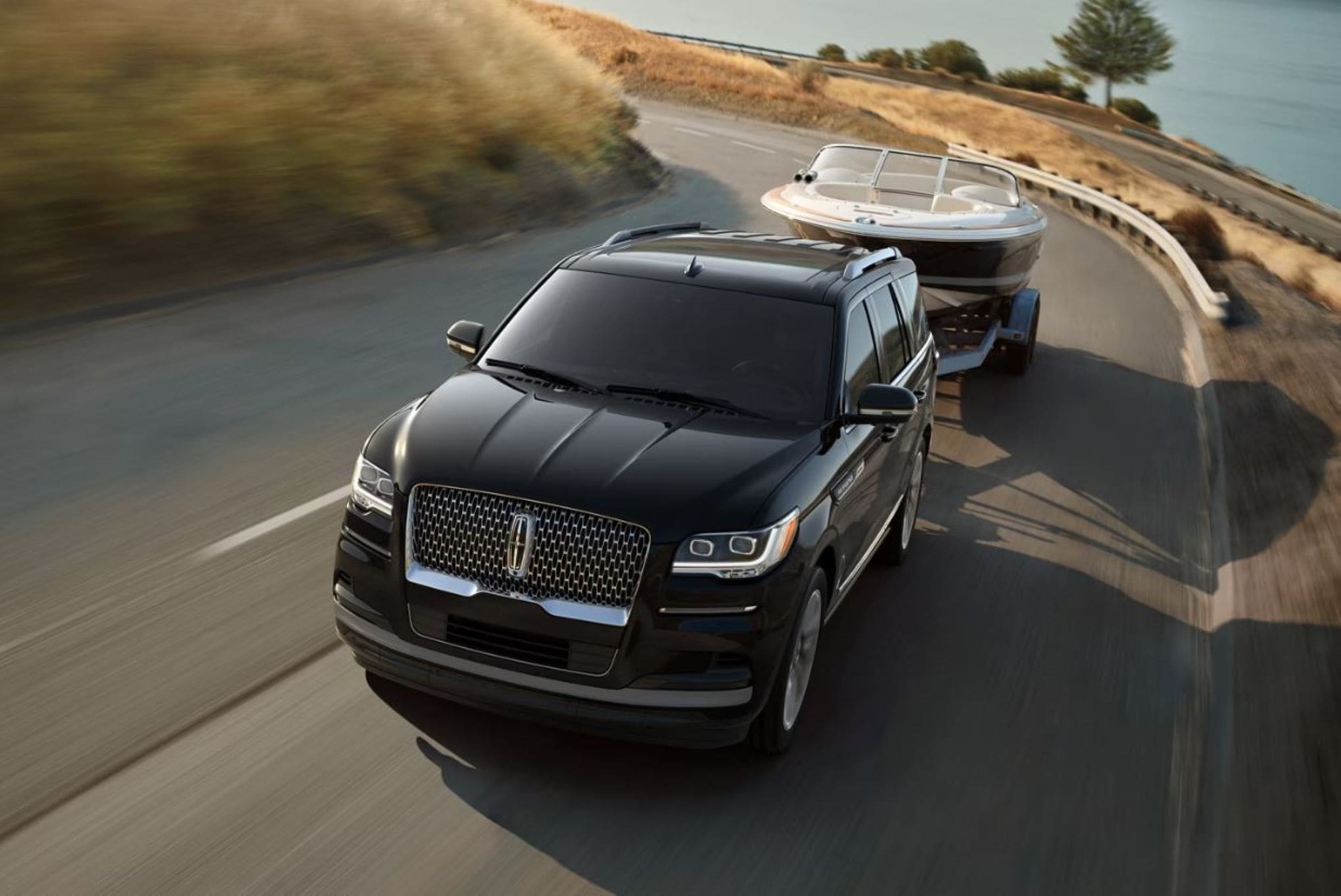 A Lincoln Navigator towing a boat on a road near a lake shore.