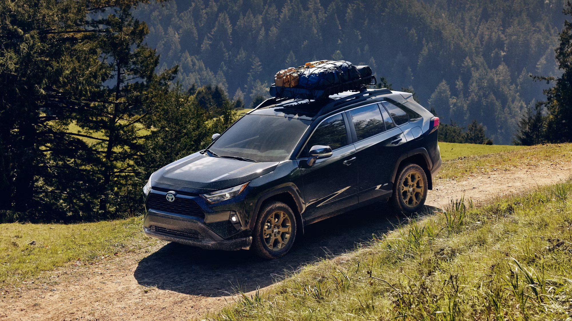 A black 2024 RAV4 drives on a dirt road in the mountains.