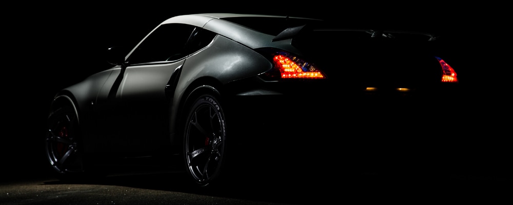 Dark image of a used sports car coupe in a dark garage with a single spotlight shining above the car