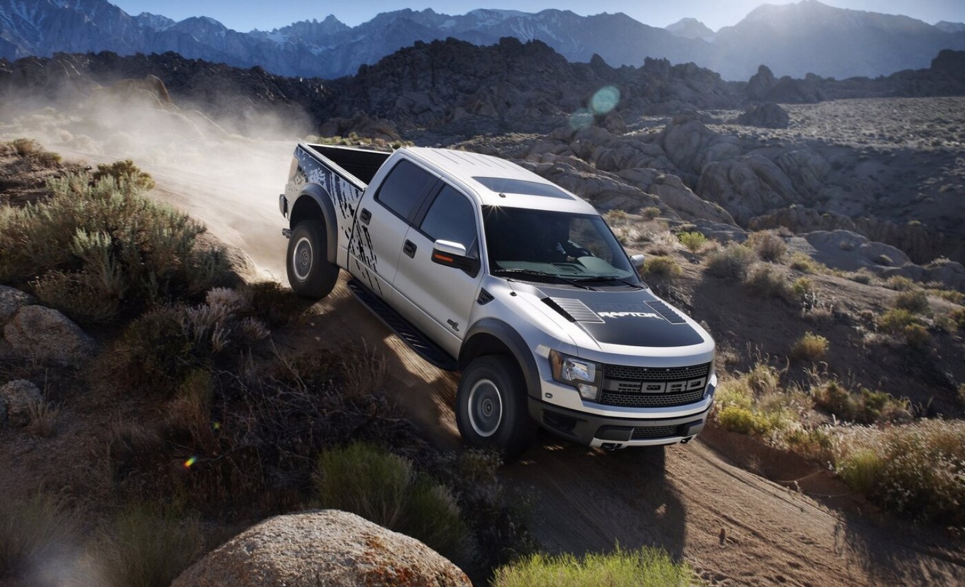 Used 2011 Ford F-150 SVT Raptor descending a dirt off-road trail with a rocky mountain range in the distance