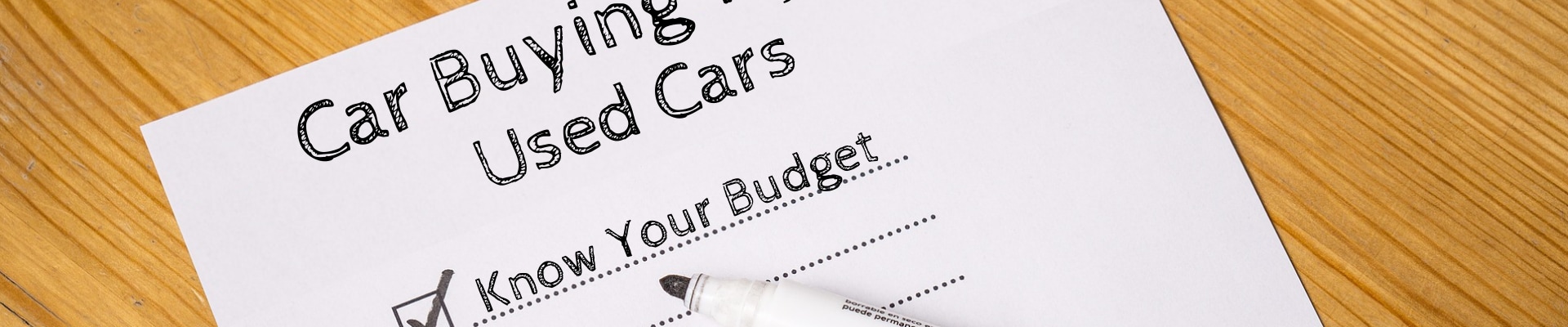 Top half of a sheet of paper on a hardwood table with a checklist of used car buying tips