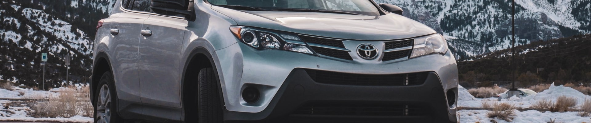 Close up angle of the front of a used Toyota RAV4 SUV parked in front of a snowy mountain range scene