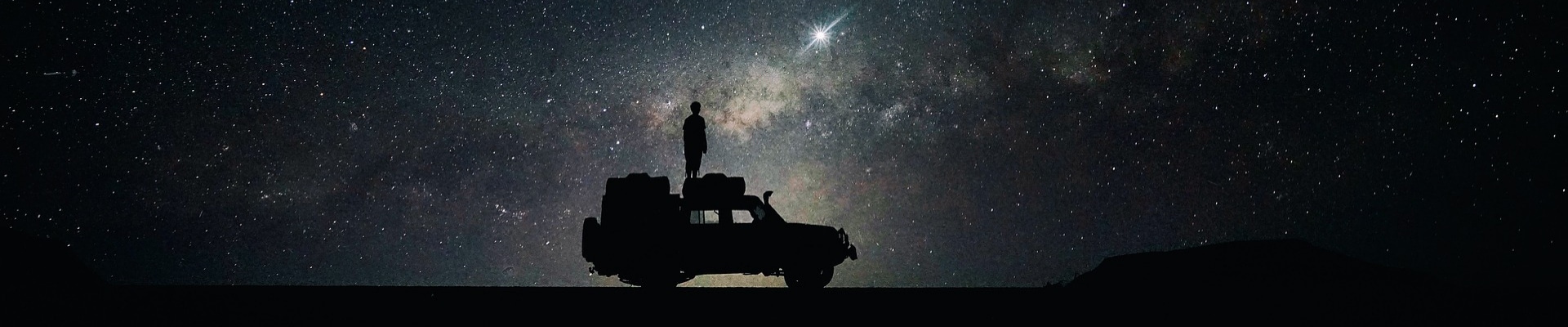 Night time sky full of stars with the silhouette of a man standing on his SUV
