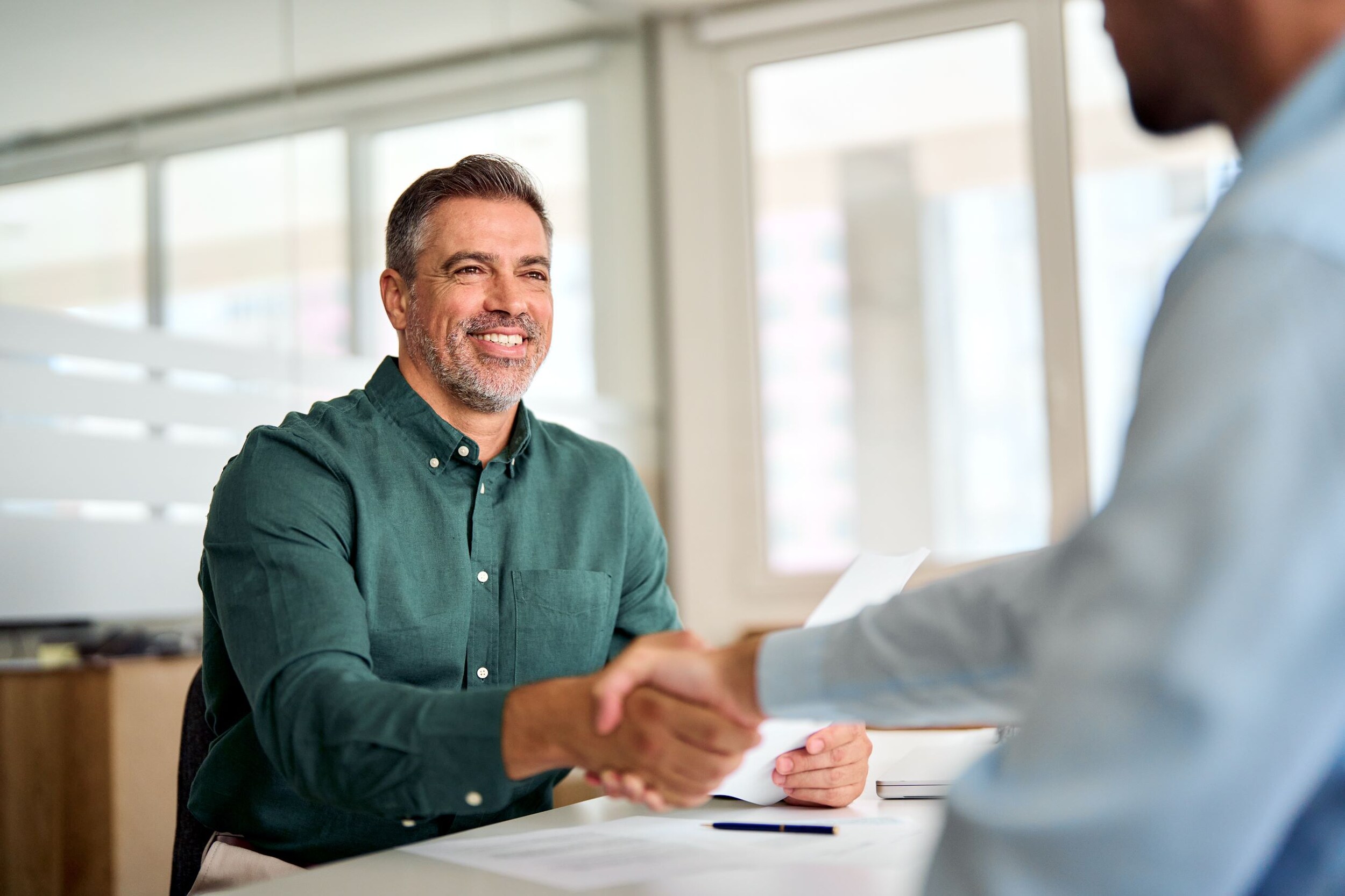 A man shaking hands with a salesperson after negotiating a deal on their trade-in.
