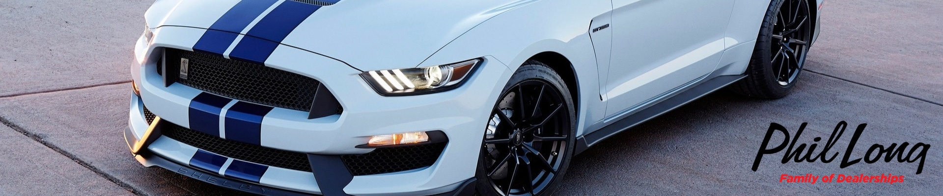 Zoomed angle on the hood of a used Ford Mustang parked in a concrete lot logo of Phil Long Dealerships in the bottom right corner