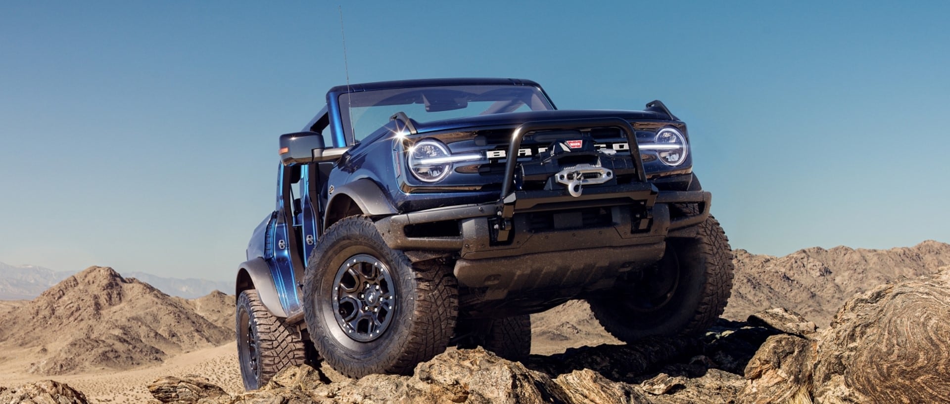 a new blue Ford Bronco driving up rocks in the desert