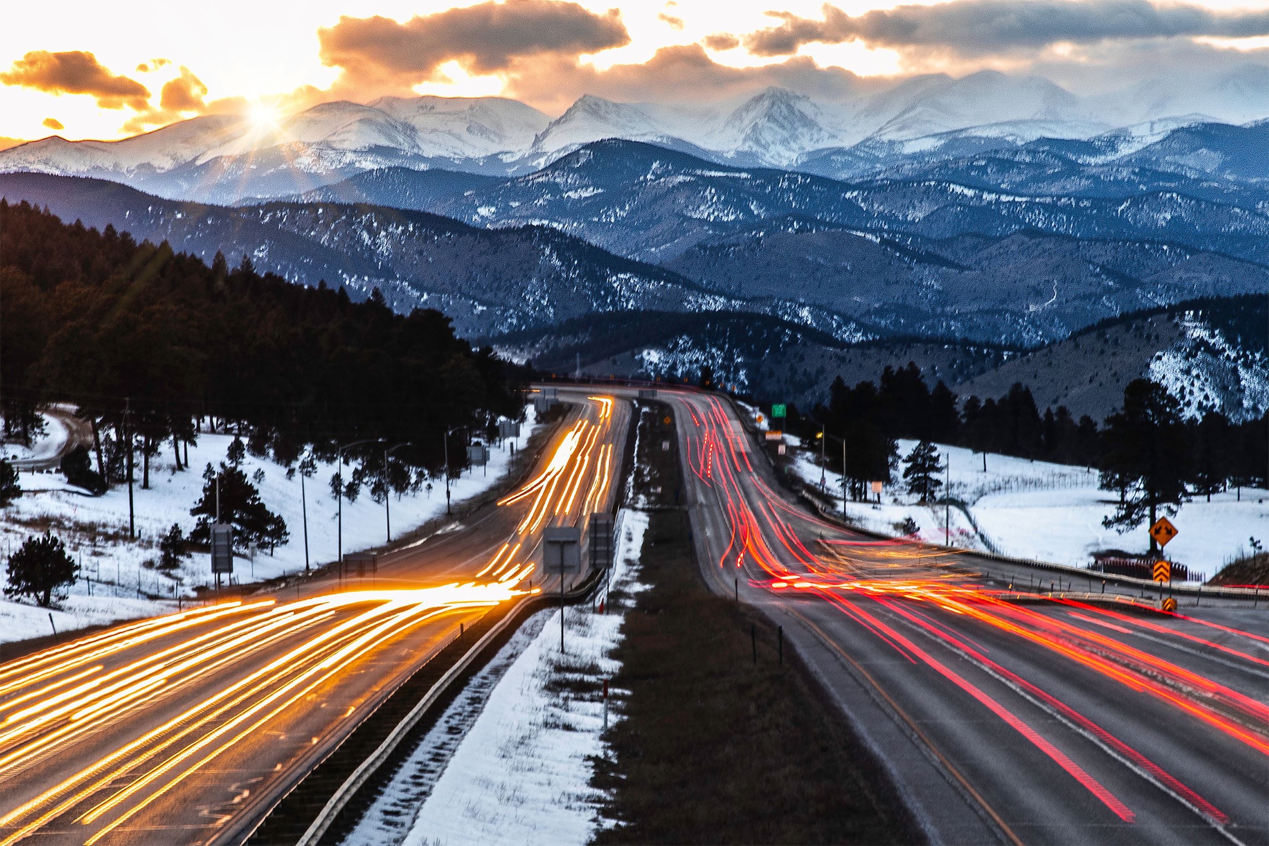 A view above I-70 looking at the mountains of Colorado with cars passing below.
