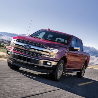 A
ruby red 2019 Ford F-150 driving down an open country road with a small
beautiful mountain range in the background