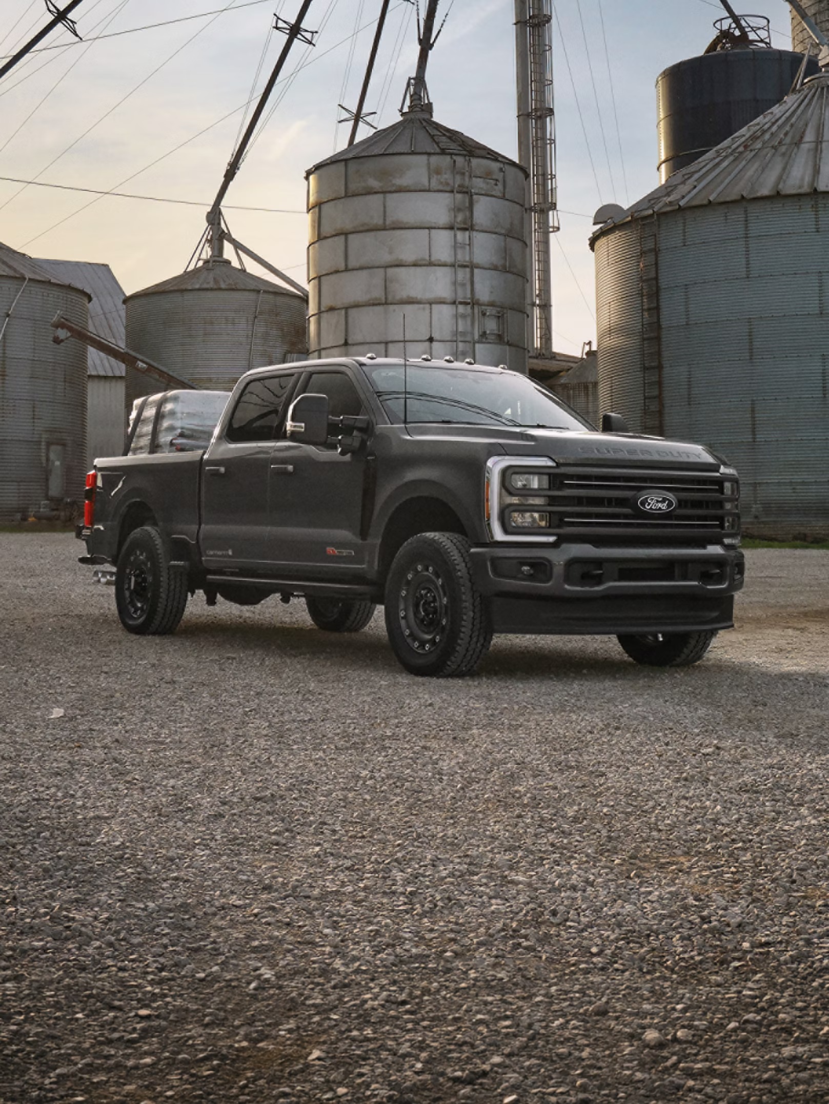 Black Ford Super Duty F-250 pickup parked by grain silos on a farm