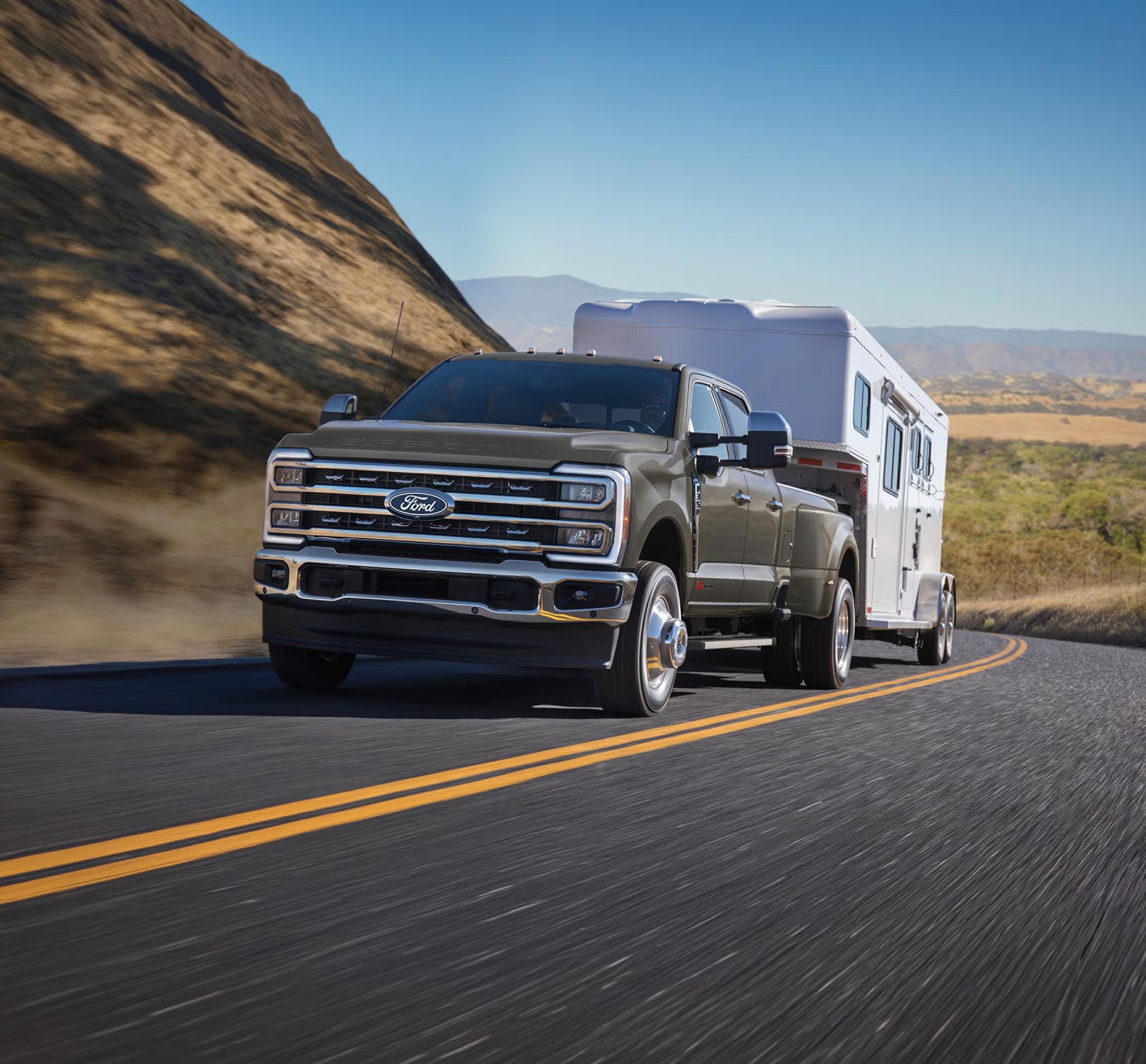 Ford F-450 Super Duty dual-rear-wheel pickup towing a travel trailer on a mountain road